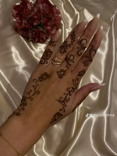 a woman's hand with henna tattoos on it and flowers in the background