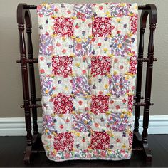 a red and white quilt is hanging on a wooden stand in front of a wall