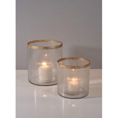 two clear glass candle holders with gold rims on the sides, one holding a lit candle