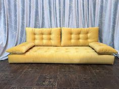 a yellow couch sitting on top of a hard wood floor next to a blue curtain