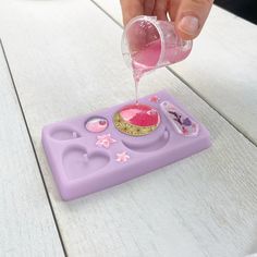 a person is pouring pink liquid on a purple play food set with hearts and stars