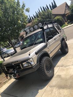 an off - road vehicle parked on the sidewalk in front of a house with several cars behind it