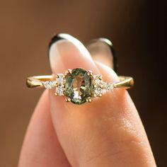 a woman's hand holding a ring with an oval green stone and three small diamonds