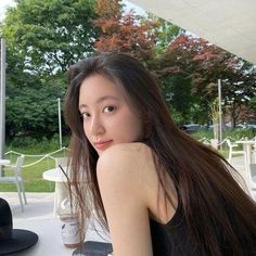 a woman sitting at a table with her long hair blowing in the wind and looking into the camera