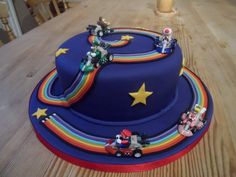 a birthday cake decorated with toy cars and rainbows on a wooden table in a kitchen