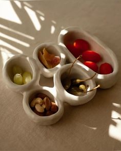 four bowls filled with different types of fruits and nuts on top of a white table