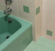 a green bath tub sitting next to a white tiled bathroom wall in a public restroom