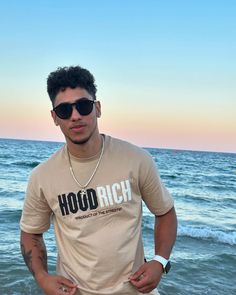 a man standing on the beach with his hands in his pockets wearing sunglasses and a t - shirt that says hod rich