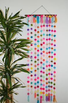 a potted plant sitting next to a wall hanging with colorful pom - poms