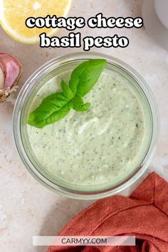 a small glass bowl filled with pesto and topped with fresh basil leaves next to an orange slice