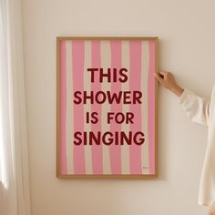 a woman standing in front of a pink and white striped poster that says, this shower is for singing