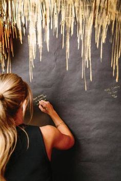 a woman writing on a blackboard with gold foiled streamers hanging from it