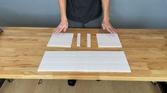 a person standing at a wooden table with two white squares on it and one black square in the middle