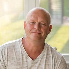 a bald man sitting in front of a window