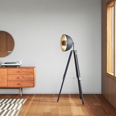 a lamp on a tripod stands next to a dresser