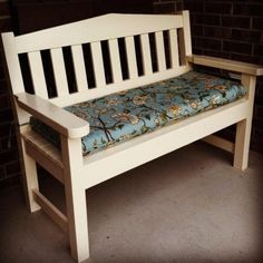 a white bench with a blue flowered seat cushion sitting in front of a brick wall