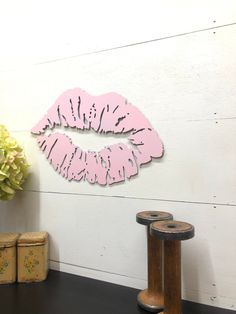 a wooden sign with pink lipstick on it next to a vase and two small jars