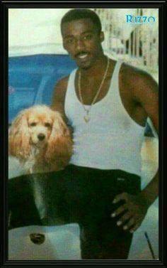 a man in white tank top standing next to a brown and white poodle dog