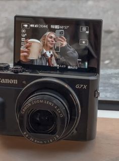 a digital camera sitting on top of a wooden table next to a window with an image of a woman holding a coffee cup