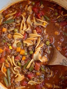 a large pot filled with pasta and meat soup on top of a wooden spatula