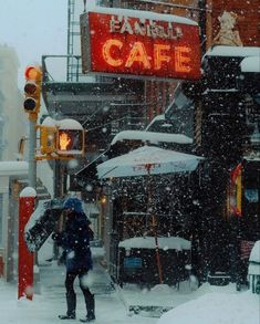 a person with an umbrella is walking in the snow near a cafe on a snowy day