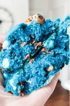 a person holding up a cookie with blue icing and chocolate chip cookies on it