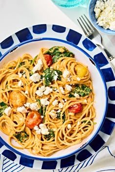 pasta with tomatoes, spinach and feta cheese in a blue and white bowl