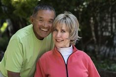 a man and woman are posing for a photo in front of some trees with their arms around each other