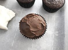 three chocolate cupcakes with frosting on a table next to some other pastries