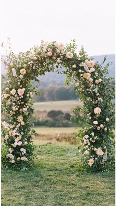 an outdoor wedding arch decorated with white flowers and greenery in the middle of a field