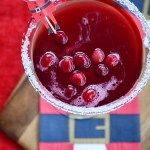 a drink in a glass with ice and cranberries on the rim, sitting on a checkered tablecloth