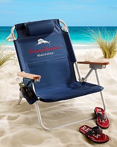 a blue beach chair sitting on top of a sandy beach next to an umbrella and flip flops