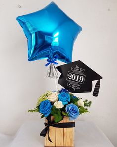 blue balloons and flowers in a wooden crate with graduation cap on the top that reads 2019