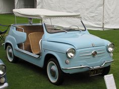 an old blue car parked on top of a lush green field next to a white tent