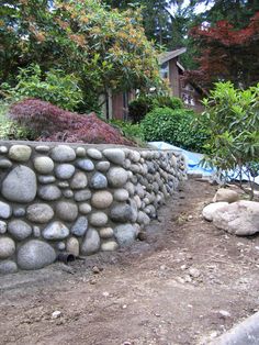 a stone wall in the middle of a yard with trees and bushes behind it,