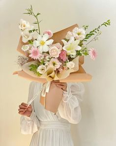 a woman holding a bouquet of flowers on her face and wearing a white dress with long sleeves