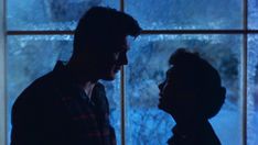 two people standing next to each other in front of a window with snow on it