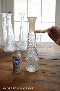 a person is painting glass vases on a wooden table with an acrylic brush