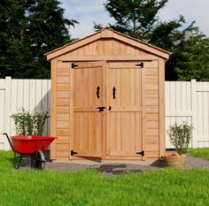 a garden shed with a wheelbarrow next to it and a red wagon in the yard