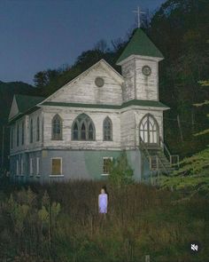 a woman standing in front of an old white church at night with the moon behind her