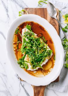 a white bowl filled with food on top of a wooden cutting board next to a spoon