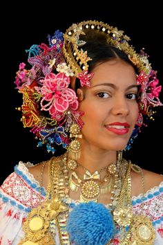 a woman with many necklaces and flowers on her head, holding a blue pom - pom