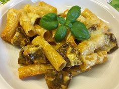 a white plate topped with pasta and meat covered in sauce, garnished with green leaves