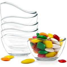 a glass bowl filled with lots of candy next to a stack of plastic spoons