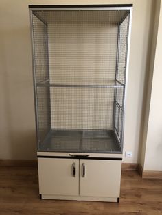 a white cabinet with two doors and some wire on the top, next to a wooden floor