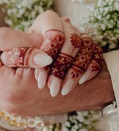 two hands holding each other with henna tattoos on their palms and fingers, while surrounded by flowers