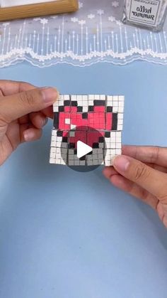 two hands are holding an origami piece that looks like a face and has been made out of squares