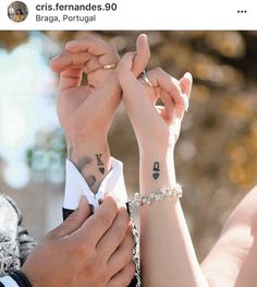 two people holding hands with tattoos on their arms and wristbands, both wearing rings