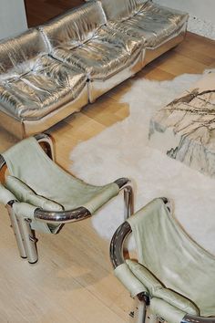 two silver leather chairs sitting on top of a hard wood floor next to a couch