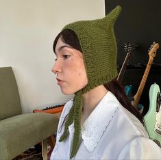 a woman wearing a green knitted hat and scarf with an electric guitar in the background